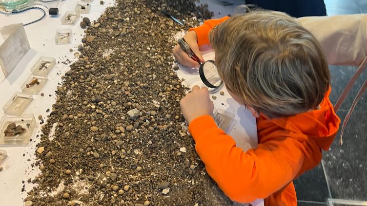Kind zoekt met vergrootglas in aarde naar archeologische resten