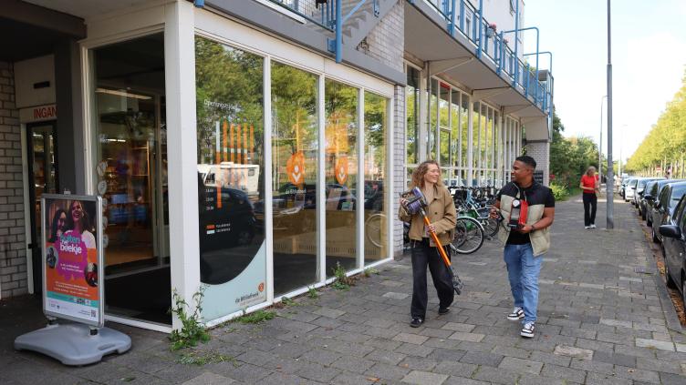 2 mensen lopen op straat met een stofzuiger en koffiezetapparaat in hun handen voor hergebruik
