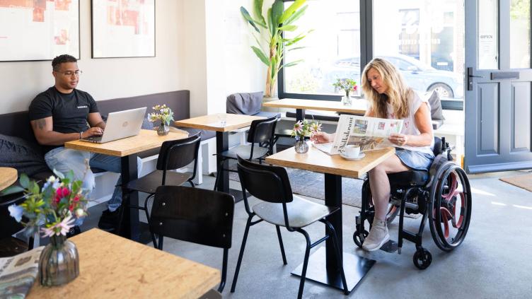 Een vrouw in een rolstoel leest de krant en een man kijkt naar een laptop