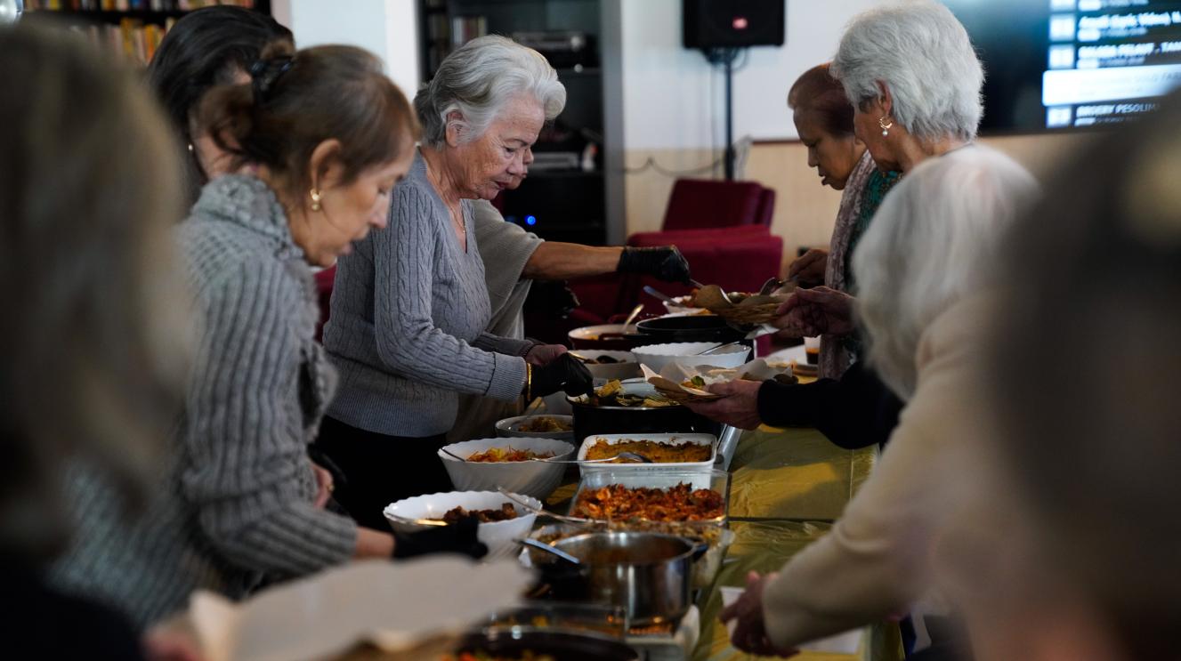 Ouderen scheppen eten voor elkaar op bij een buffet tafel