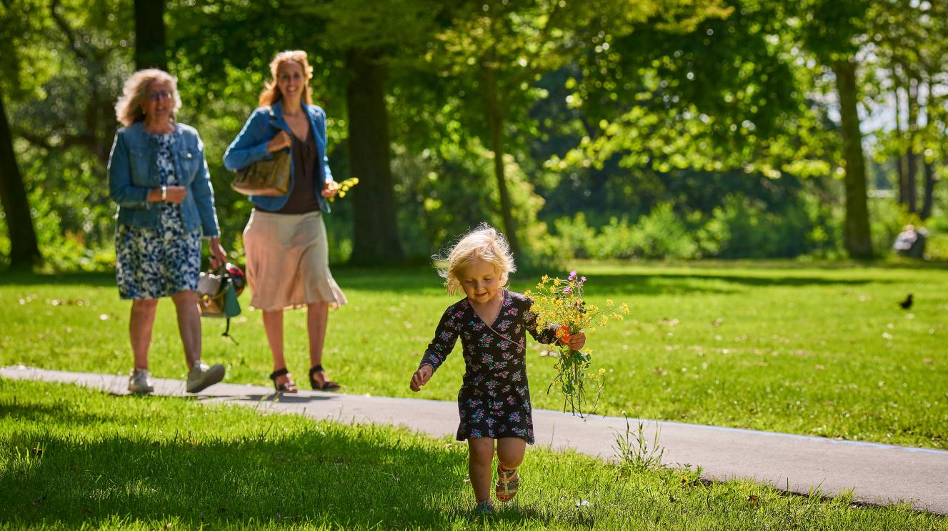 Oma, moeder en een klein kindje met een bosje bloemen in haar hand lopen in het Schoterbos op een zonnige dag