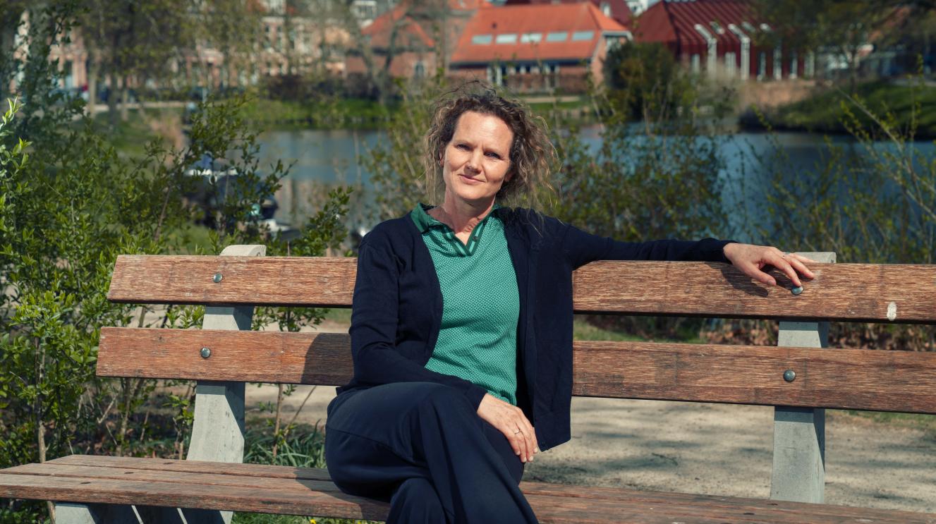 Portetfoto van Hanneke Kijne. Zij zit op een bankje aan het water.