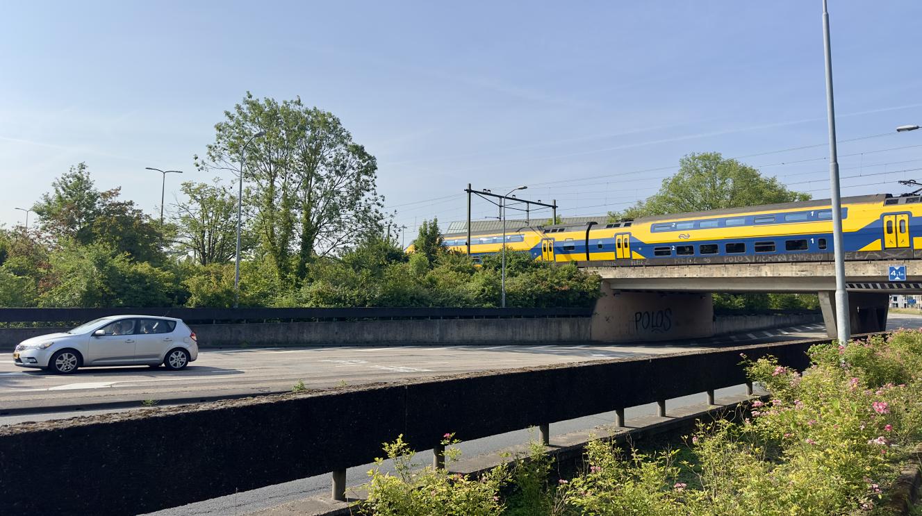 Asfaltweg met auto en rechts een spoorbrug met een trein erop