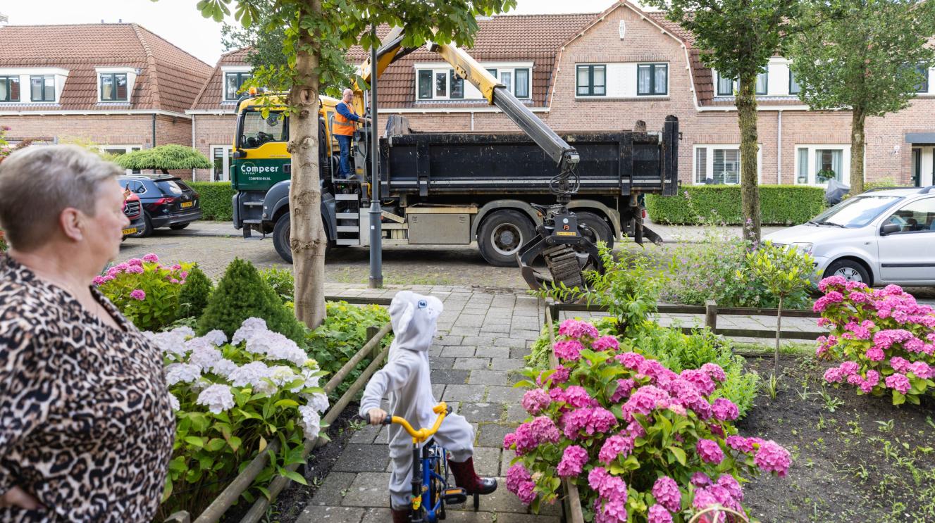 Vrouw en kindje kijken hoe de tegeltaxi tegels optakelt