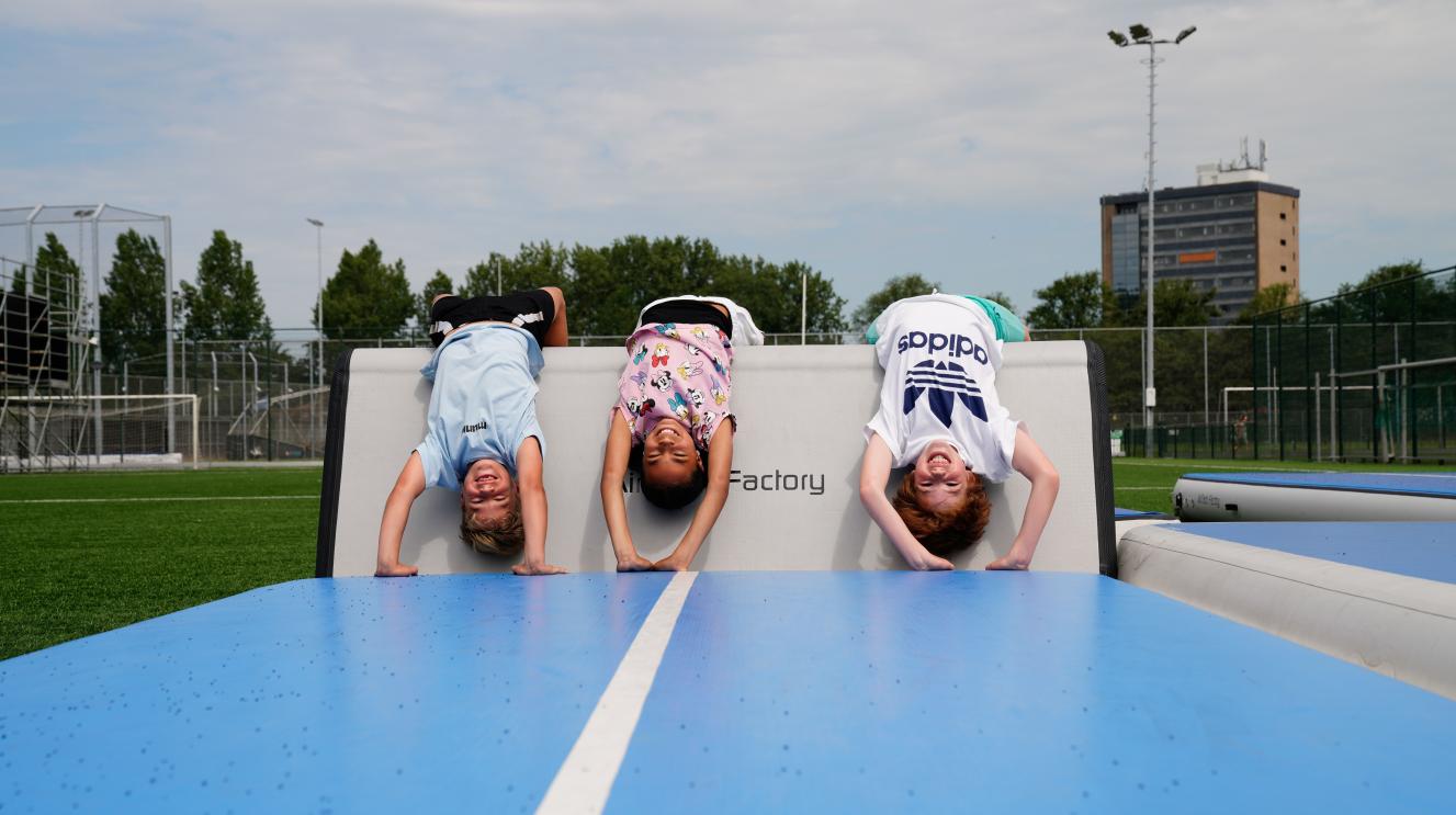 Drie kinderen op een luchtkussen voor turnen, die lachen in de camera.