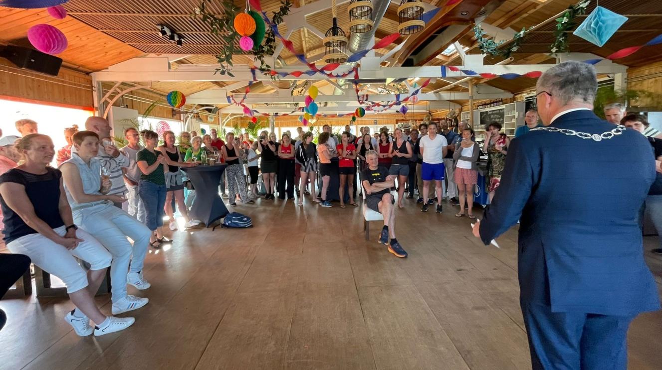 Mensen in een ruimte in een halve kring die luisteren naar burgemeester Wienen