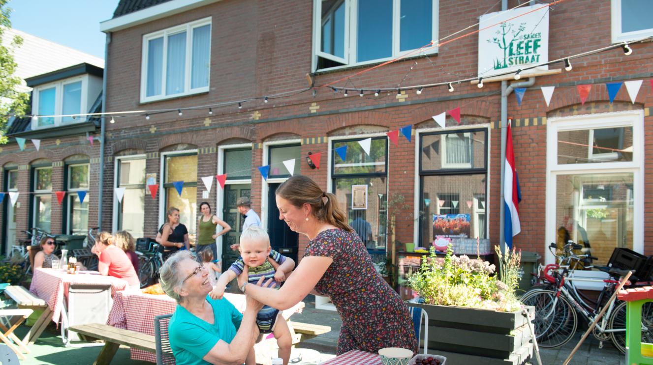 Mensen, waaronder twee vrouwen en een baby, zitten aan een tafel op straat, die is omgetoverd tot een leefstraat.