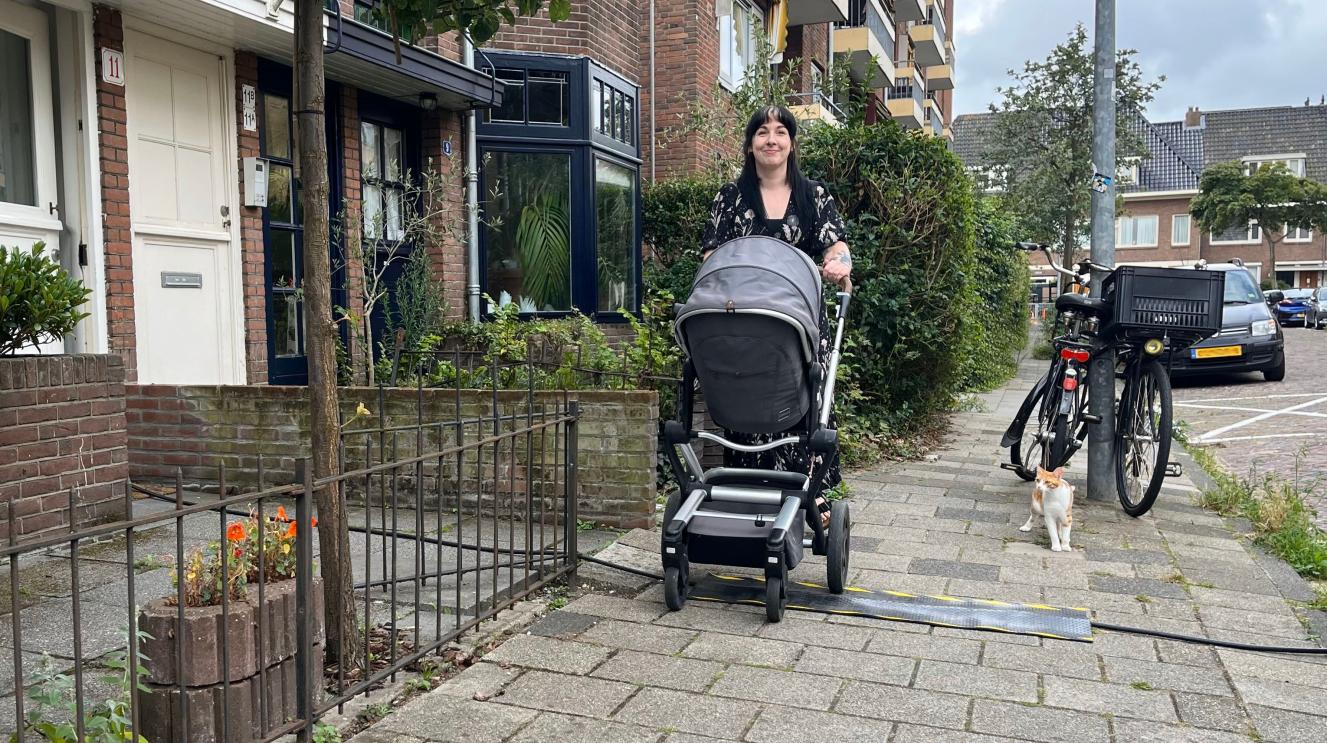 Vrouw met kinderwagen loopt richting een kabelmat op de stoep.