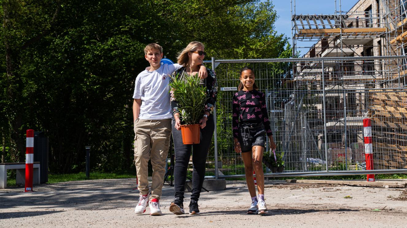 Een jongen, een vrouw en een meisje lopen op straat met planten