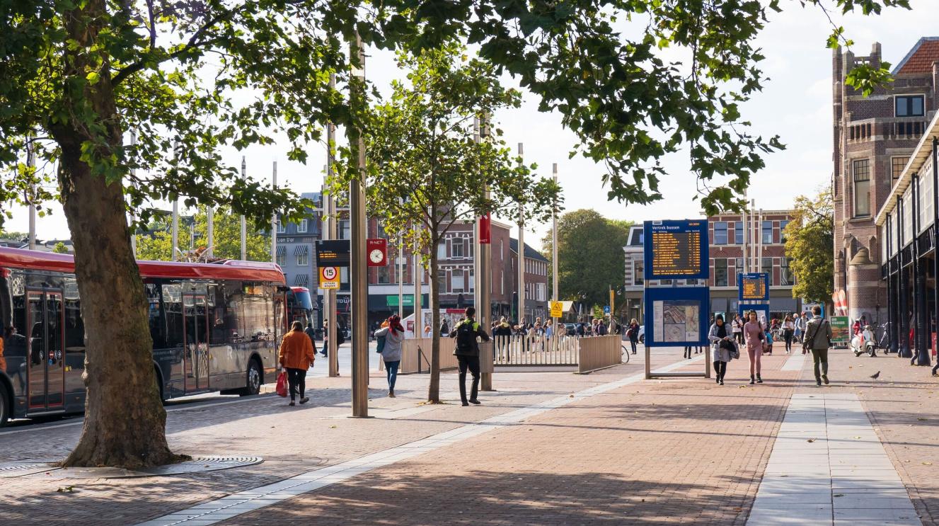 Het stationsplein in de zomer, met een bus en voetgangers