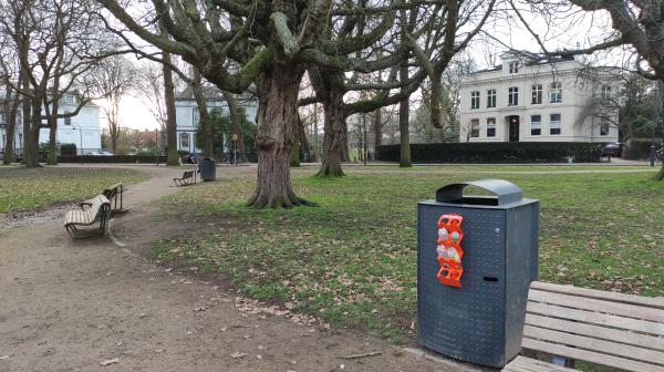 Afvalbak met doneerrekje voor petflesjes naast een bankje in een park