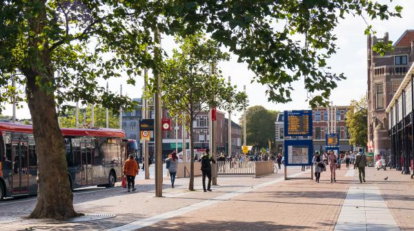 Het Stationsplein met een bus en wandelende mensen 