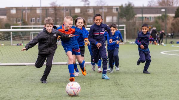 Jongeren rennen achter een bal aan op het voetbalveld van Olympia. Foto door Jurriaan Hoefsmit