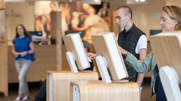 Foto van personen die in de publiekshal gebruik maken van het digitale scherm.