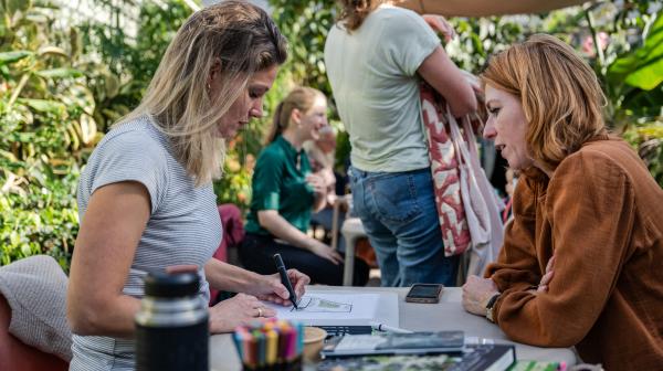 Twee vrouwen bekijken aan een tafeltje buiten een schetsontwerp